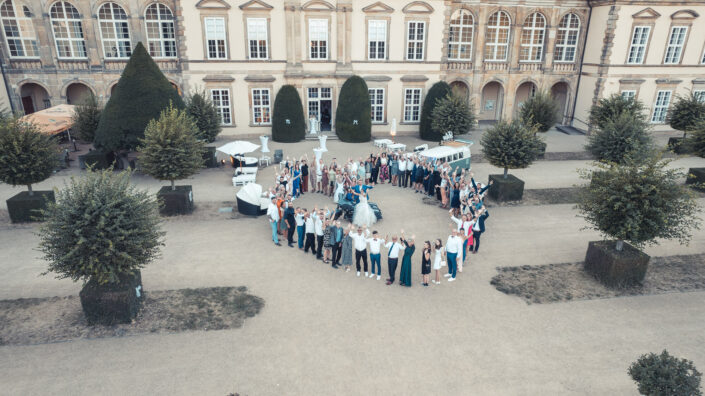 Das Brautpaar steht mit allen Hochzeitsgästen für ein Gruppenfoto zusammen, fotografiert von Christian Roder