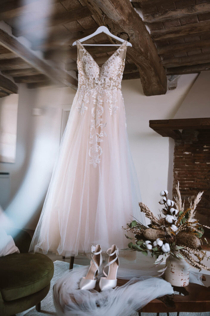 Aufnahme vom hängenden Brautkleid und den Brautschuhen und dem Schleier auf einem dekorativen Holztisch