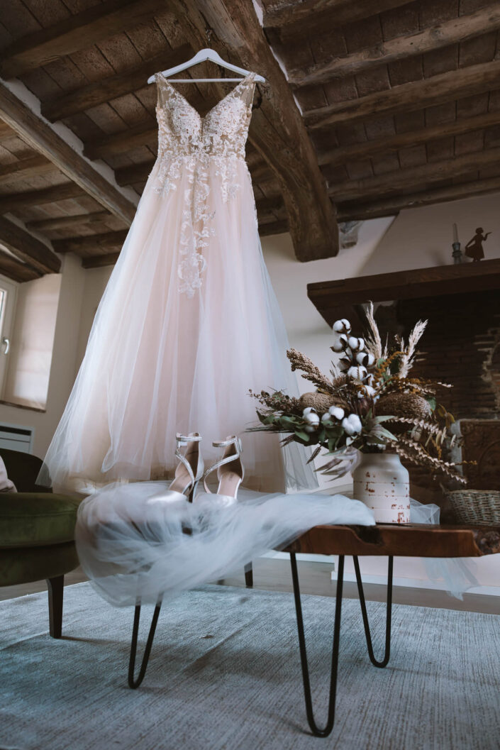 Aufnahme vom hängenden Brautkleid und den Brautschuhen und dem Schleier auf einem dekorativen Holztisch