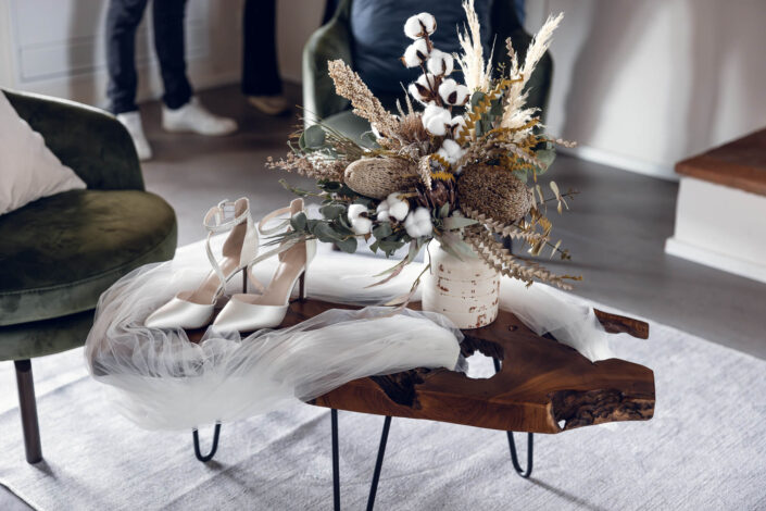 Nahaufnahme von den Brautschuhen und dem Schleier auf einem dekorativen Holztisch