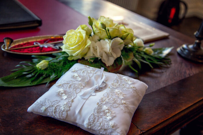 Zwei Eheringe liegen auf einem weißen Hochzeitskissen, fotografiert von Christian Roder