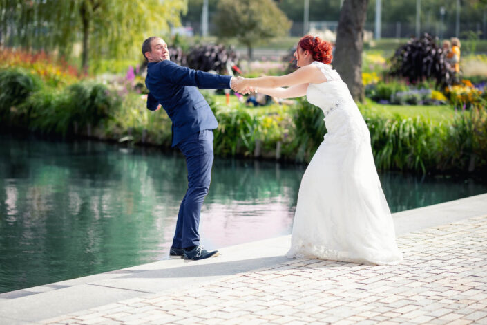 Die Braut hält den Bräutigam fest, der beinahe ins Wasser fällt – humorvoller Moment, fotografiert von Christian Roder