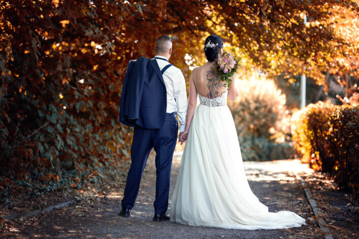 Braut und Bräutigam gehen Hand in Hand durch die Natur, von hinten fotografiert von Christian Roder