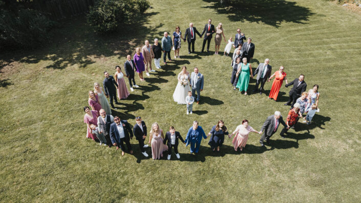 Die gesamte Hochzeitsgesellschaft von oben fotografiert, mit dem Brautpaar im Zentrum